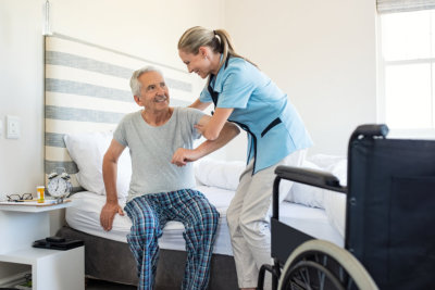 Smiling nurse assisting senior man to get up from bed
